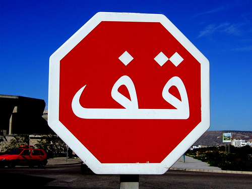 Señal de stop octogonal roja con la palabra árabe «قف» en blanco, bajo un cielo azul intenso