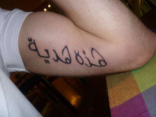 Brazo con el tatuaje «هذه هدية» («esto es un regalo») en letras negras sobre el bíceps